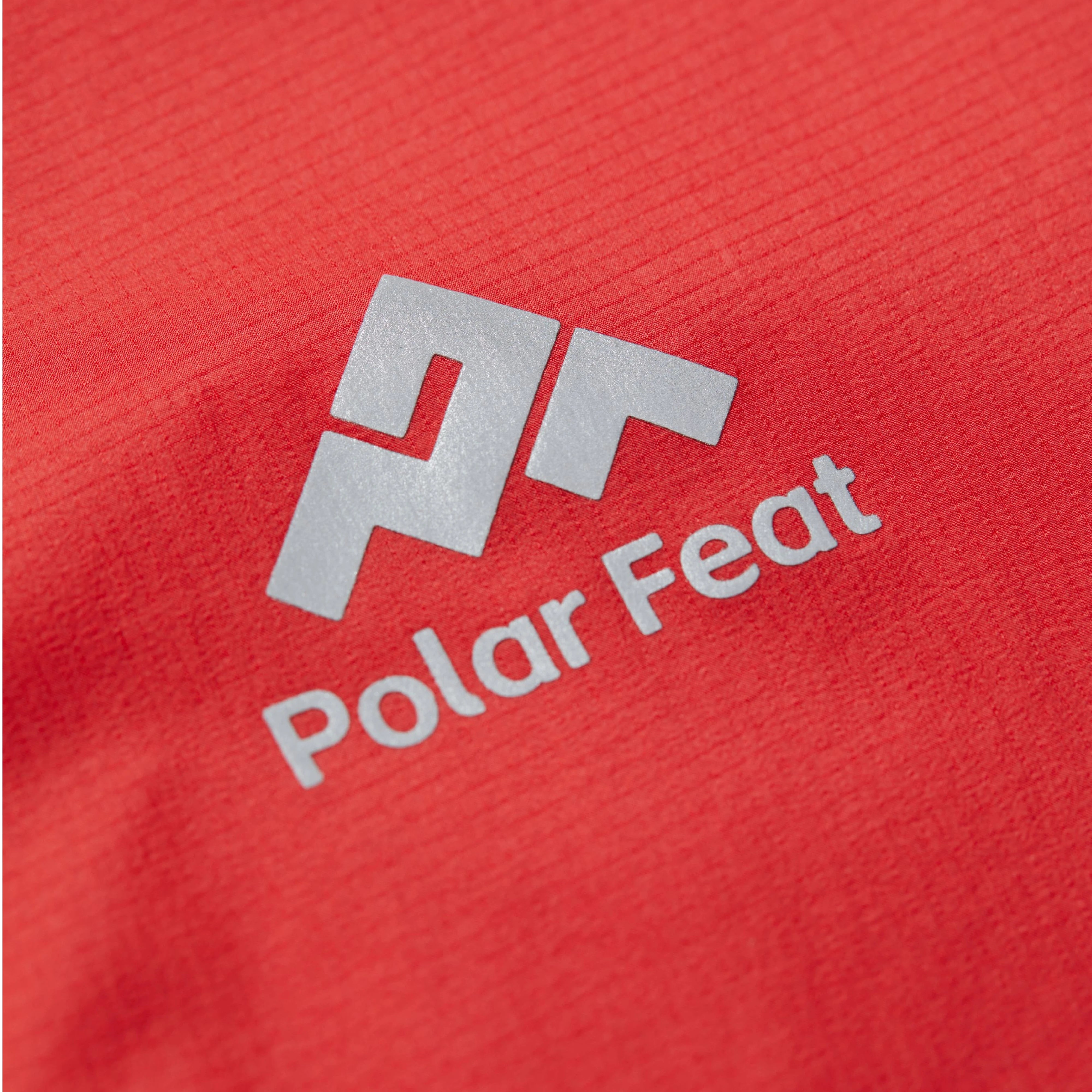 Close-up of a red fabric surface with a silver 'Polar Feat' logo.